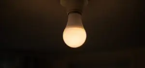 A white smart light bulb glowing dim and warm in a bare ceiling socket
