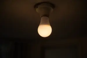 A white smart light bulb glowing dim and warm in a bare ceiling socket