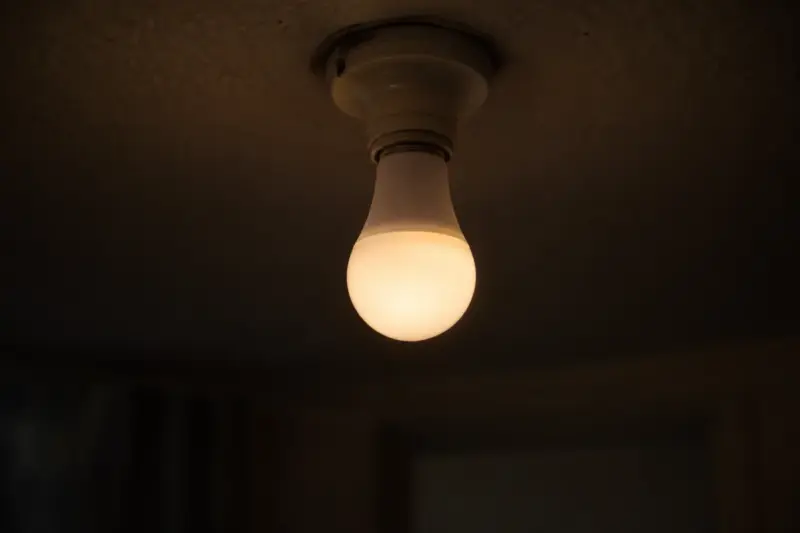 Why Philips Hue Bulbs Buzz, and How to Stop It A white smart light bulb glowing dim and warm in a bare ceiling socket